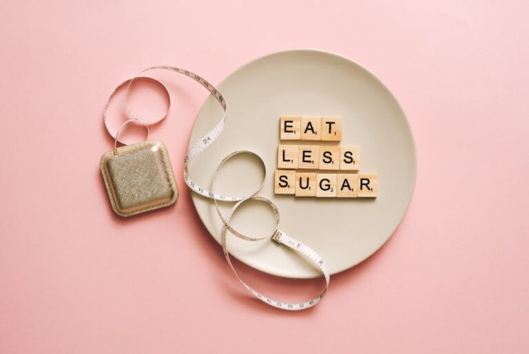 Flat lay of Scrabble tiles saying 'Eat Less Sugar' on a plate with a tape measure on a pink background.